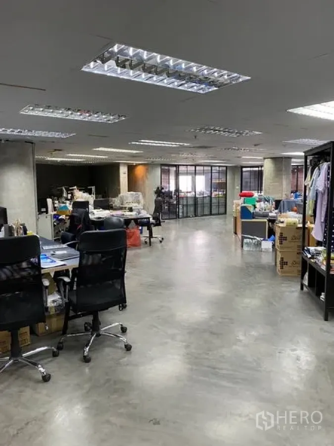 Office Space for rent in Khlong Toei, Bangkok - Open-plan office with polished concrete floors, ample fluorescent lighting, desks and shelving, and a glass-partitioned area at the far end.