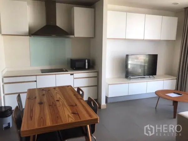 Condominium for rent in Watthana, Bangkok - Open-plan kitchen with dining table, cooktop, range hood and TV unit in the living space.