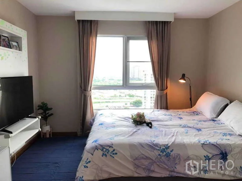 Condominium for sale in Huai Khwang, Bangkok - Bright master bedroom with large window, city view, TV and bedside lamp.