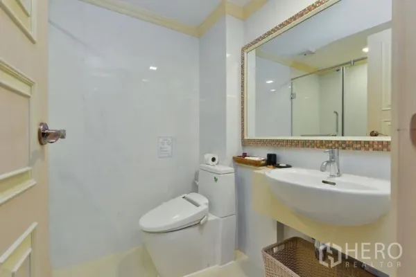 Apartment for rent in Khlong Toei, Bangkok - Bright bathroom with large mirror, vanity sink, toilet and glass shower enclosure.