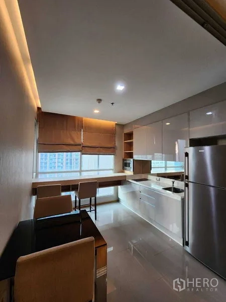 Condominium for sale in Ratchathewi, Bangkok - Open kitchen and dining area with full-size fridge, microwave, glossy cabinetry and city-facing windows.