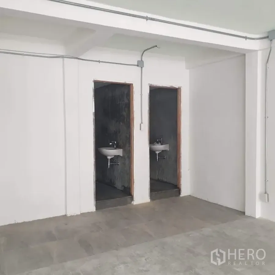 Home Office for rent in Khlong Toei, Bangkok - Two minimalist restrooms with white wall-mounted sinks and raw concrete walls.