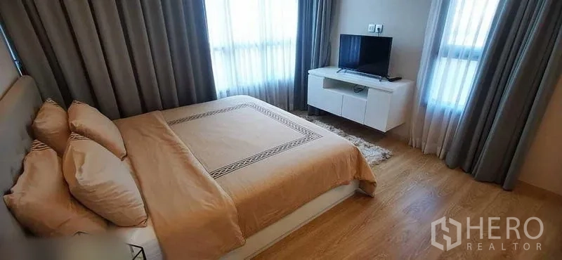 Condominium for rent in Watthana, Bangkok - Bright bedroom with queen bed, TV console and two large curtained windows on wood flooring.