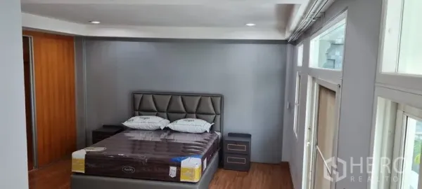 Townhouse for rent in Watthana, Bangkok - Master bedroom with padded headboard, bedside tables, and wood flooring.