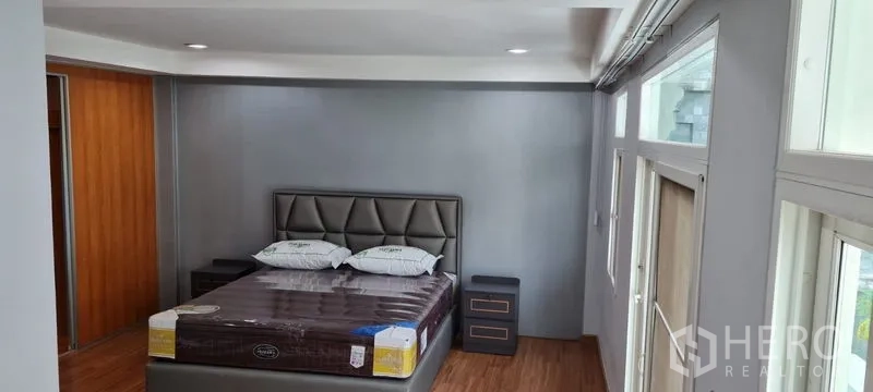 Townhouse for rent in Watthana, Bangkok - Master bedroom with padded headboard, bedside tables, and wood flooring.