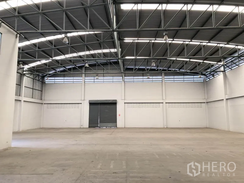工厂 出租在Pathum Thani - 高挑拱形钢结构仓库内景，带卷闸门与采光
