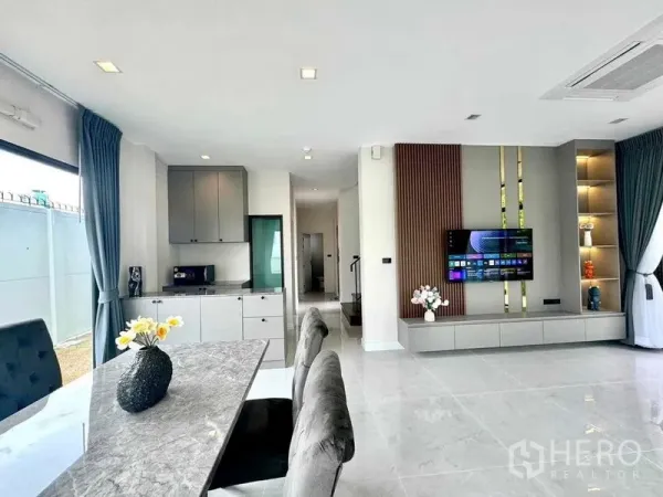 Detached House for rent or sale in Bang Phli, Samut Prakan - Open-plan dining and kitchenette with marble table, built-in TV wall, floor-to-ceiling windows and glossy tile floors.