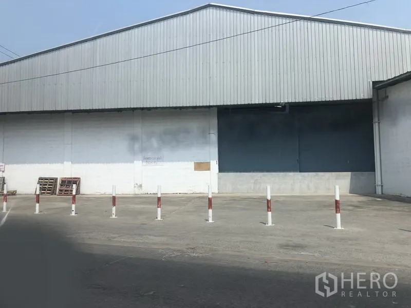 Warehouse for rent in Nonthaburi - Large warehouse exterior with loading bay door, safety bollards and a wide paved yard.