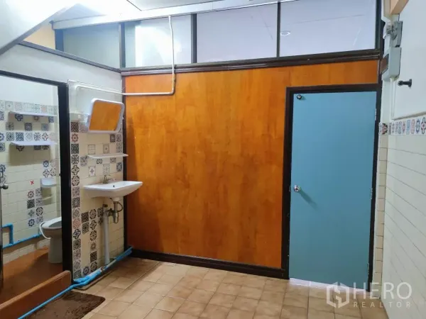 零售空间 出租在Watthana, Bangkok - 后部区域，木色墙面、蓝色门与瓷砖地，旁有洗手盆