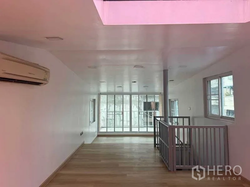 Shophouse for rent in Bang Rak, Bangkok - Bright mezzanine level with air-conditioning, stairwell balustrade, and sliding glass wall to a balcony.