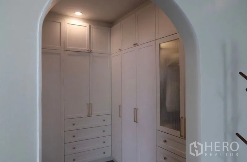 Detached House for rent or sale in Saphan Sung, Bangkok - Walk-in closet with built-in white cabinetry and drawers under an archway.