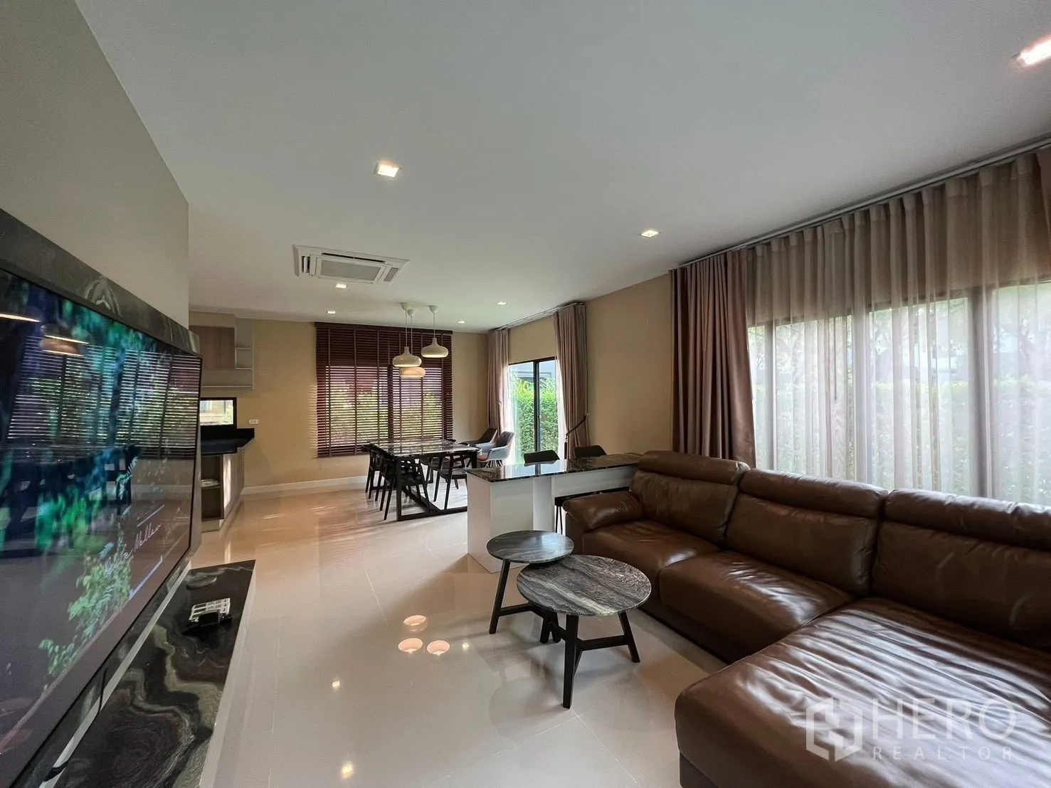 Detached House for rent in Bang Phli, Samut Prakan - Open-plan living room with a large leather sectional sofa, TV feature wall, and floor-to-ceiling windows.
