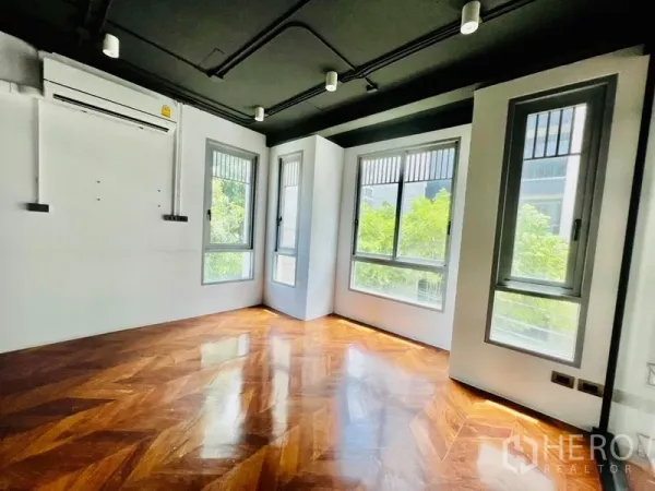 Office Space for rent in Khlong Toei, Bangkok - Corner office room with herringbone wood floor, black ceiling and multiple windows facing trees.
