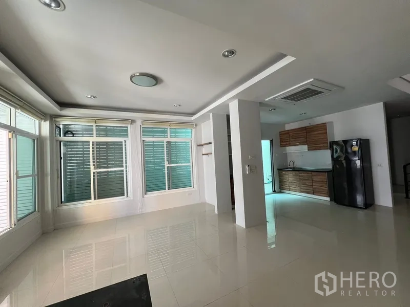 Townhouse for rent in Din Daeng, Bangkok - Open-plan living and kitchen area with large windows, glossy tiles and wood cabinets with black fridge.