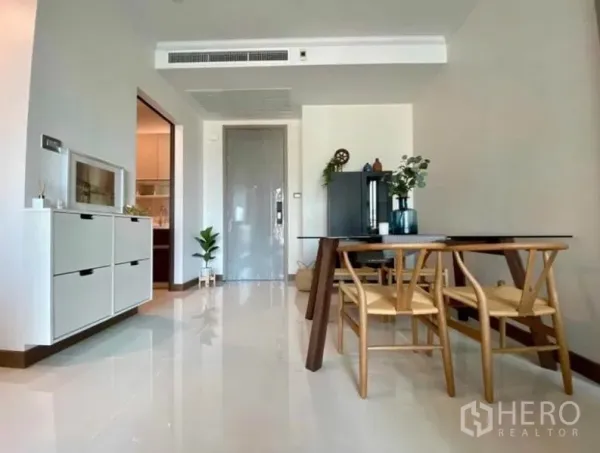 Condominium for rent in Watthana, Bangkok - Minimalist dining area with wooden table and chairs, glossy tile floors and entry door.