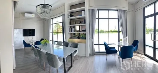 Detached House for rent in Bang Phli, Samut Prakan - Bright dining and sitting area featuring floor‑to‑ceiling windows, chandelier lighting and built‑in shelving.