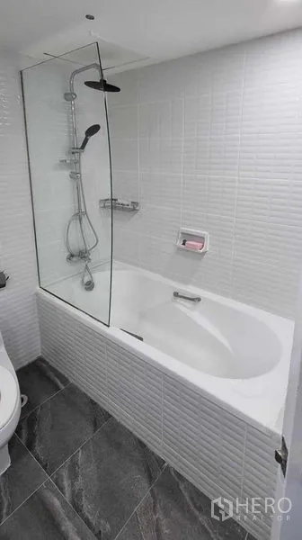 公寓 出租在Khlong Toei, Bangkok - 浴室为白色瓷砖，设玻璃隔断的浴缸与淋浴系统。