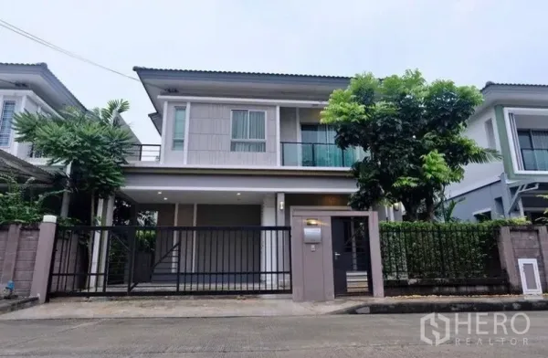 Detached House for rent in Suan Luang, Bangkok - Two-storey detached house exterior with gated carport, balcony, and mature tree in a quiet Suan Luang lane.
