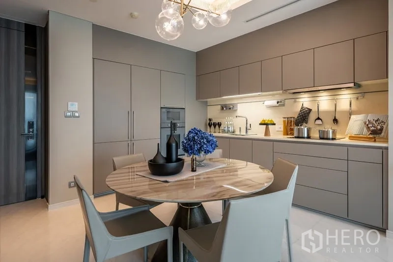 Condominium for rent or sale in Pathum Wan, Bangkok - Sleek built-in kitchen with dining set and designer chandelier.