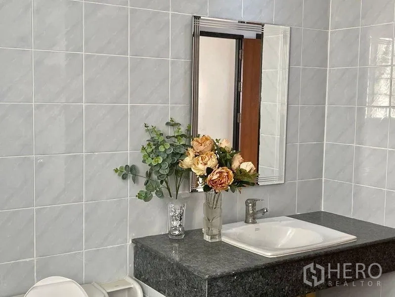 Home Office for rent - Bathroom vanity with mirror, gray tiles and decorative flowers.