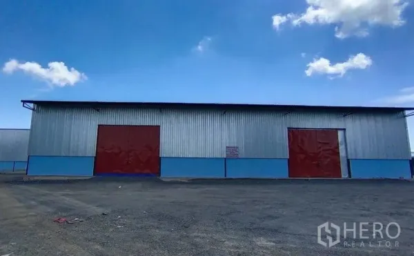 Warehouse for rent in Si Racha, Chon Buri - Warehouse exterior with corrugated metal walls, two red sliding doors, and wide yard.