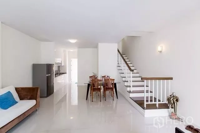 Townhouse for rent in Watthana, Bangkok - Bright open-plan living and dining area with glossy white floors and staircase.