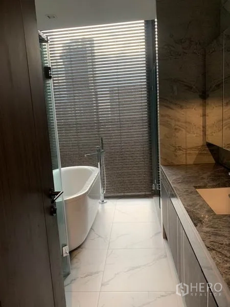 Condominium for rent in Watthana, Bangkok - Bathroom with freestanding bathtub by the window, marble-style walls and a long vanity.