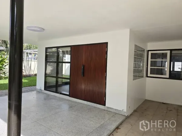 บ้าน ให้เช่าในWatthana, Bangkok - เฉลียงและโรงจอดรถในร่ม ประตูไม้บานใหญ่และหน้าต่างกรอบอลูมิเนียมดำ