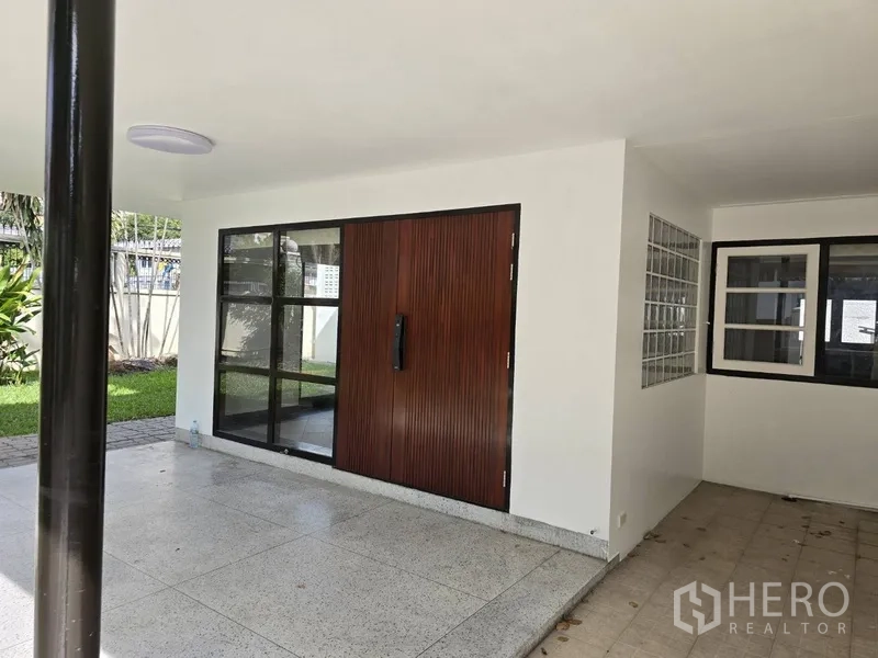 บ้าน ให้เช่าในWatthana, Bangkok - เฉลียงและโรงจอดรถในร่ม ประตูไม้บานใหญ่และหน้าต่างกรอบอลูมิเนียมดำ