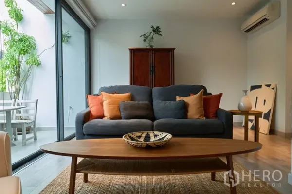 联排别墅 出租在Watthana, Bangkok - 温馨客厅，灰色沙发与彩色抱枕，推拉门通向露台。