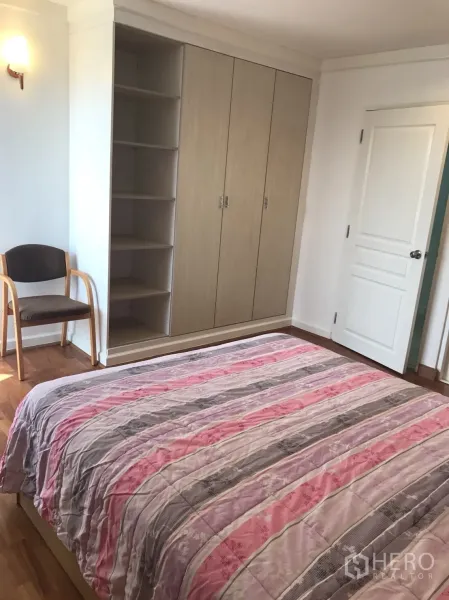 Condominium for rent in Khlong Toei, Bangkok - Primary bedroom showing built-in wardrobes with open shelving and a chair.