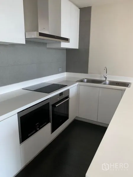 Condominium for rent in Watthana, Bangkok - Modern U-shaped kitchen with white cabinetry, built-in oven and electric cooktop.
