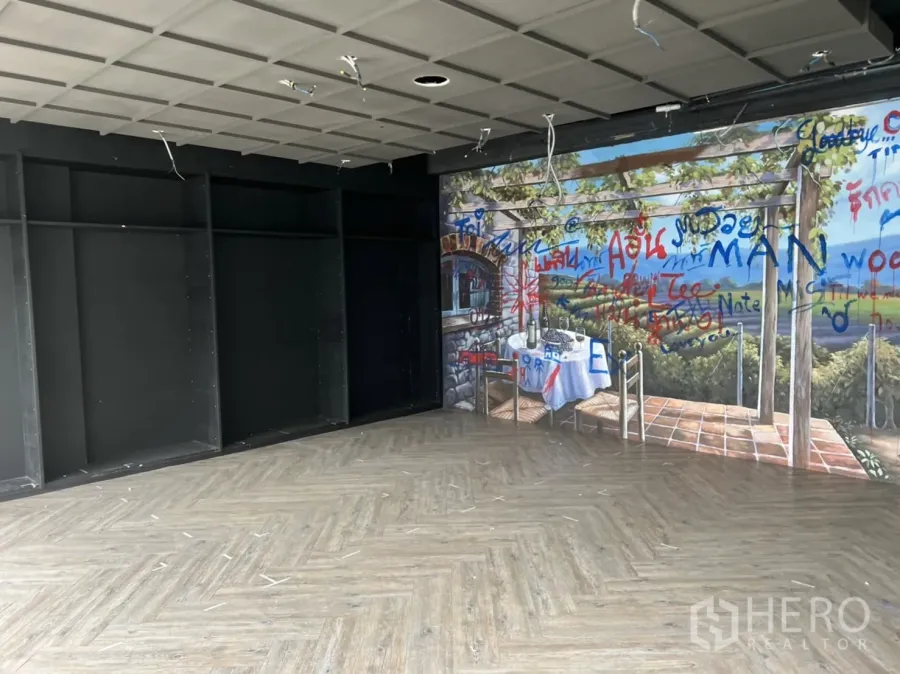 零售空间 出租在Khlong Toei, Bangkok - 空置零售室，鱼骨纹地板、深色柜架与墙面壁画，天花裸露线路。