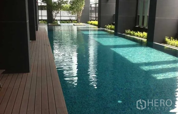 Condominium for rent or sale in Huai Khwang, Bangkok - Condominium swimming pool with wooden deck and greenery along the edge.