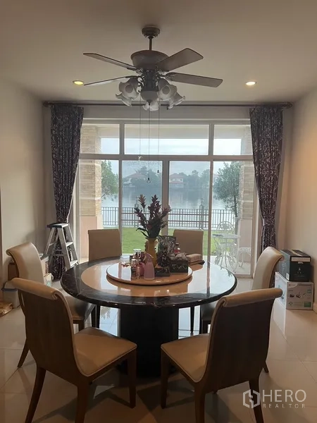 บ้าน ให้เช่าหรือขายในLat Krabang, Bangkok - มุมรับประทานอาหารโต๊ะกลม พัดลมเพดาน เปิดสู่สวนริมทะเลสาบผ่านประตูกระจกบานใหญ่.