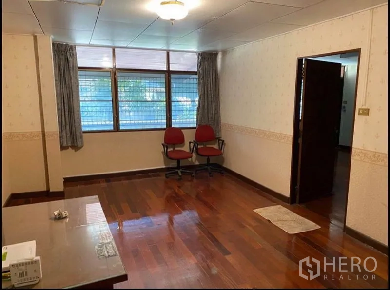Home Office for rent in Suan Luang, Bangkok - Bright room with large windows, wood flooring and two red chairs, ideal as a meeting or living area.