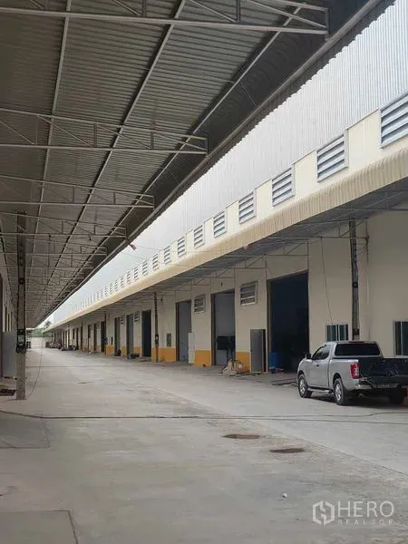 Warehouse for rent in Krathum Baen, Samut Sakhon - Covered loading bay row with large warehouse doors and vehicle access along the building.
