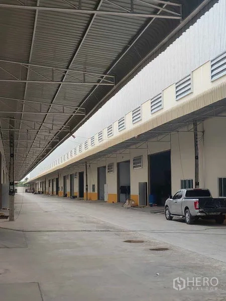 Warehouse for rent in Krathum Baen, Samut Sakhon - Covered loading bay row with large warehouse doors and vehicle access along the building.