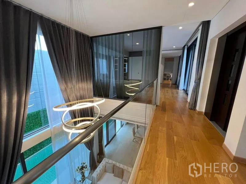Detached House for sale in Suan Luang, Bangkok - Upper corridor with glass balustrade and contemporary ring chandelier overlooking the living area.