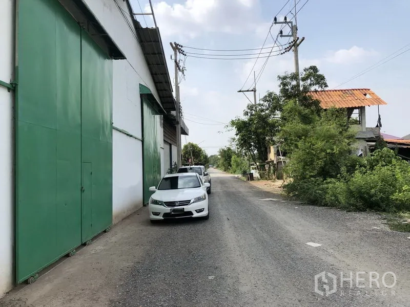货栈 出租或出售在Khlong Luang, Pathum Thani - 仓库临道路景，停放车辆、电线杆与道路绿化。