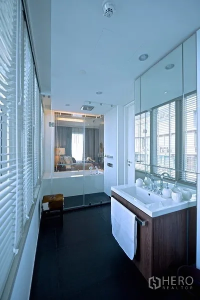 Condominium for rent in Pathum Wan, Bangkok - Modern bathroom with vanity, large mirror and glass shower enclosure with rain shower.