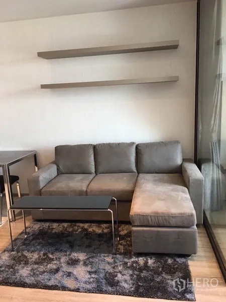 Condominium for rent in Watthana, Bangkok - Cozy L-shaped sofa in the living area with floating shelves and a rug.