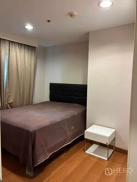 Condominium for sale in Huai Khwang, Bangkok - Compact guest bedroom with double bed, bedside table and soft lighting on wood floors.