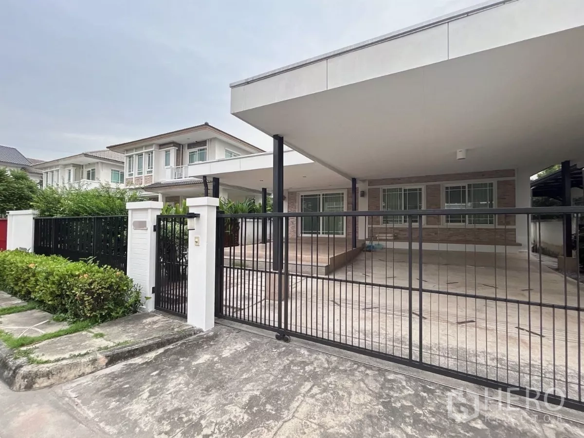 บ้าน ขายในBang Kapi, Bangkok - มุมเอียงด้านหน้าเห็นชานบ้านปูกระเบื้อง หลังคาคลุมกว้าง และแนวพุ่มไม้