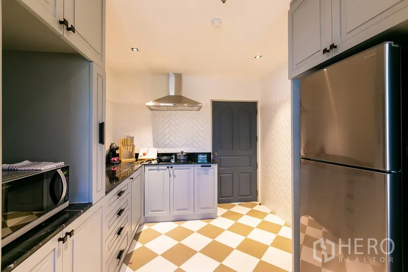 房间 出租在Khlong Toei, Bangkok - 完整厨房，灰色橱柜，棋盘格地面与不锈钢冰箱。