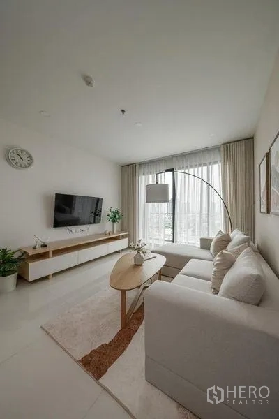 คอนโด ให้เช่าในKhlong San, Bangkok - มุมนั่งเล่นอบอุ่น มีโคมไฟโค้ง ผ้าม่านโปร่ง ชั้นวางทีวี และโทนสีเรียบหรู