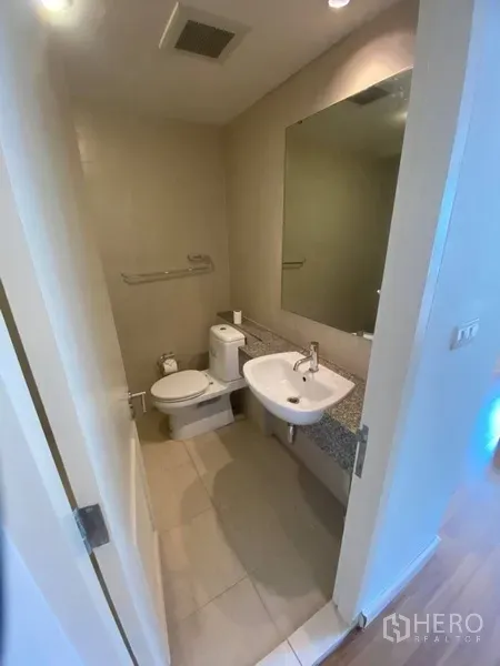 公寓 出租在Watthana, Bangkok - 紧凑卫生间，带洗手台、大镜与坐便器，色调素雅。