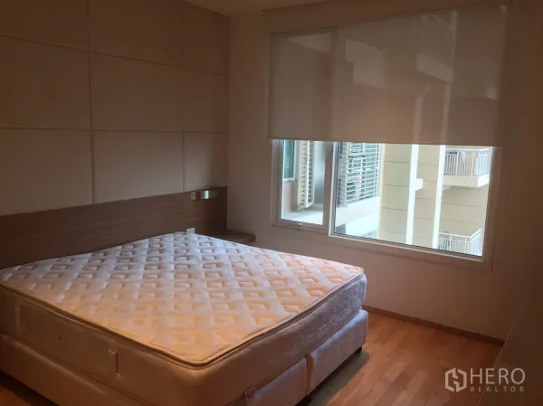 Condominium for rent in Sathon, Bangkok - Cozy bedroom with large window, roller blind, wood flooring and a queen mattress.