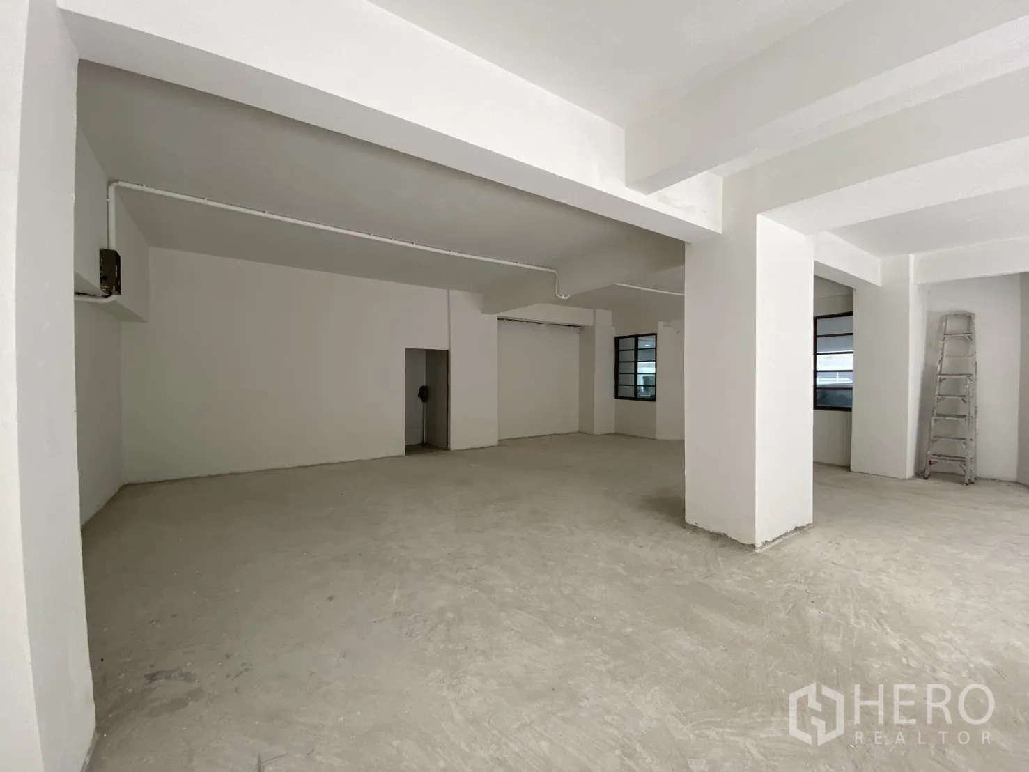 零售空间 for rent in Watthana, Bangkok - 开放式室内，白色立柱、水泥地面与后室出入口。