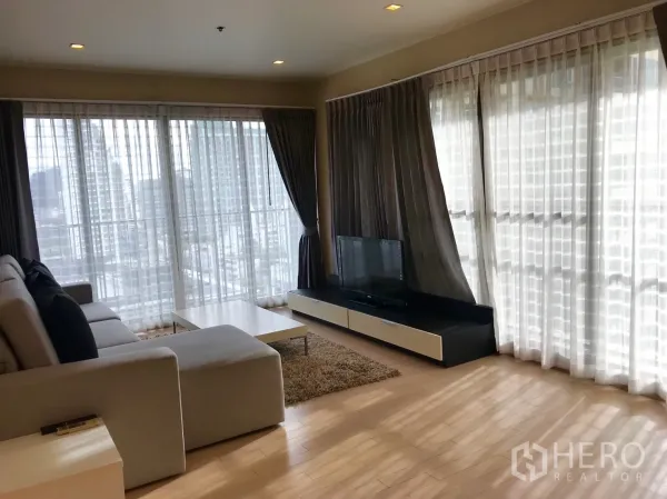 公寓 出租在Watthana, Bangkok - 转角客厅配落地窗与城市景观，电视柜、地毯与转角沙发。